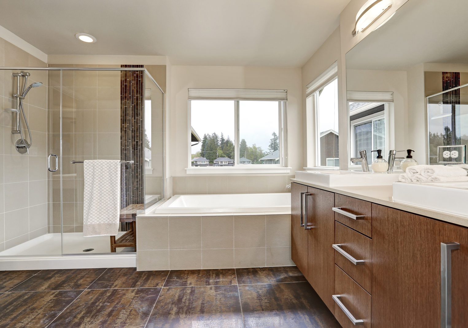 White modern bathroom interior in brand-new house. Double sink vanity with large mirror walk-in shower white bath tub and brown tile floor. Northwest USA